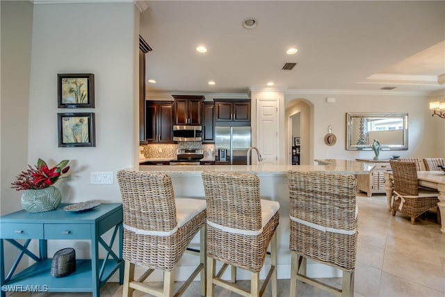 kitchen with arched walkways, a breakfast bar, stainless steel appliances, visible vents, and light stone countertops