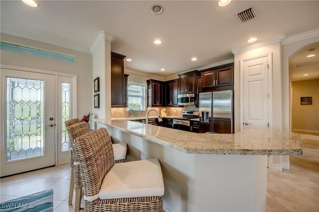 kitchen featuring ornamental molding, appliances with stainless steel finishes, a breakfast bar, and visible vents