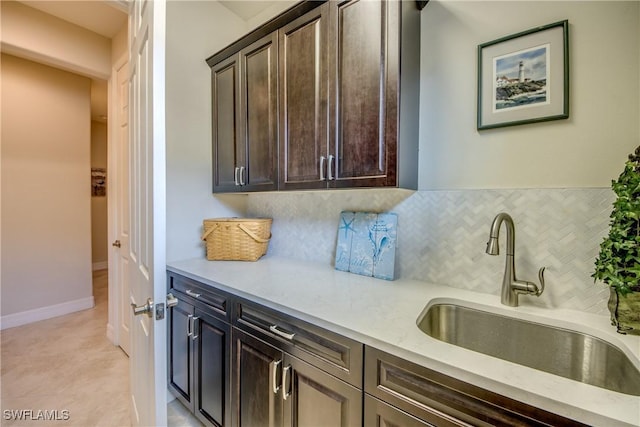 kitchen featuring backsplash, a sink, dark brown cabinetry, light stone countertops, and baseboards