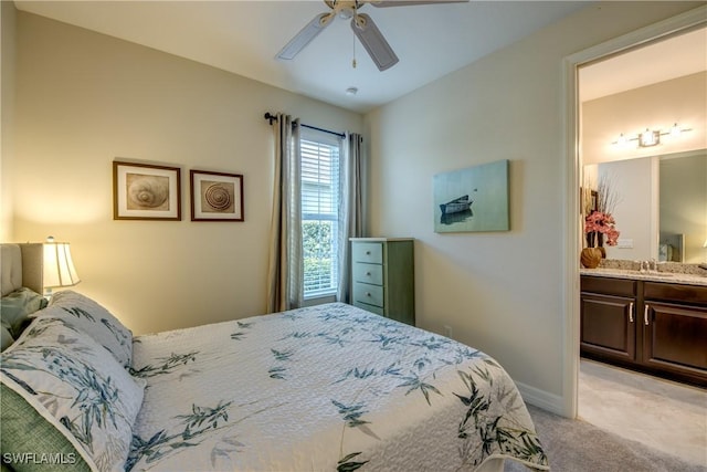 bedroom featuring light colored carpet, a sink, a ceiling fan, baseboards, and ensuite bath