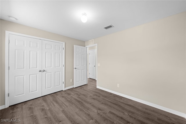 unfurnished bedroom featuring baseboards, a closet, visible vents, and wood finished floors