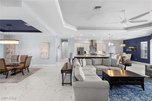 living room with a tray ceiling, marble finish floor, visible vents, and baseboards