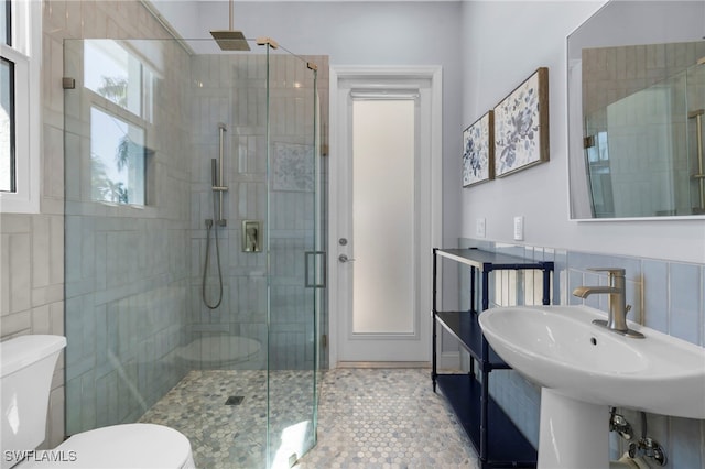 bathroom with tile walls, a sink, a shower stall, and toilet