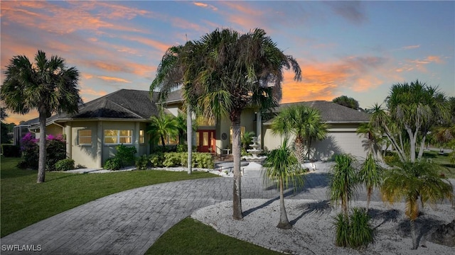 obstructed view of property with a garage, driveway, a lawn, and stucco siding