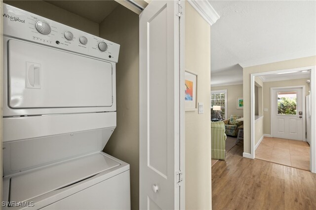 laundry room with stacked washer and clothes dryer, light wood-style floors, ornamental molding, laundry area, and baseboards