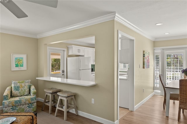 kitchen featuring white cabinets, light wood finished floors, freestanding refrigerator, and a kitchen breakfast bar