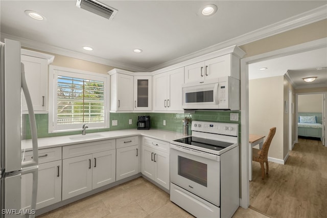 kitchen with white appliances, ornamental molding, light countertops, and a sink