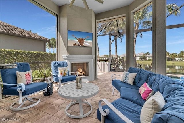 sunroom featuring ceiling fan, a lit fireplace, and a water view