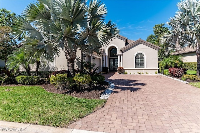 mediterranean / spanish home featuring decorative driveway, french doors, stucco siding, an attached garage, and a front yard