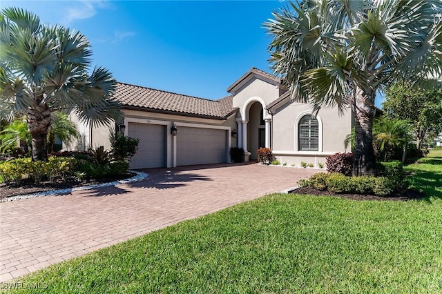 mediterranean / spanish-style house with decorative driveway, stucco siding, an attached garage, a front yard, and a tiled roof