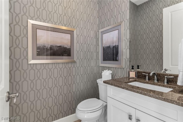 bathroom with vanity, toilet, and wallpapered walls