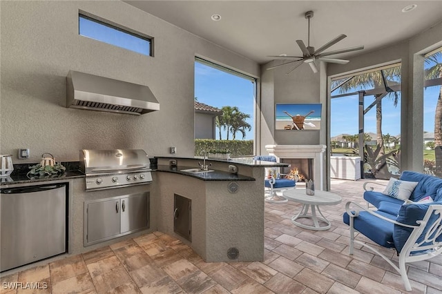 view of patio featuring ceiling fan, a grill, a lit fireplace, exterior kitchen, and a sink