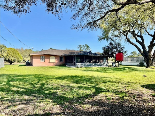 back of property with a sunroom, a lawn, fence, and stucco siding