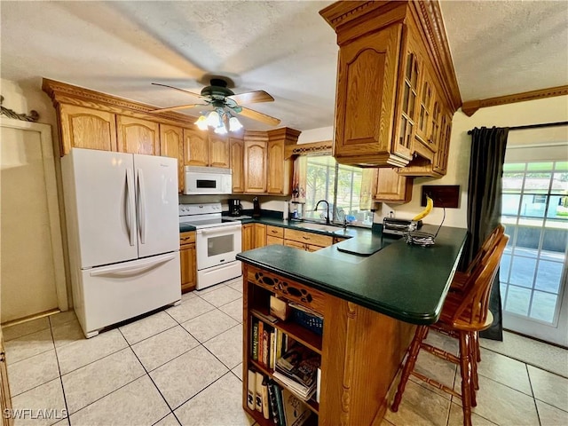 kitchen featuring light tile patterned floors, dark countertops, a sink, white appliances, and a peninsula