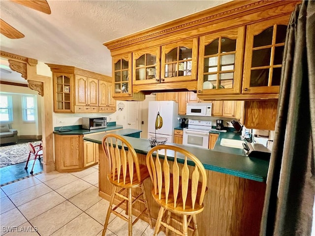 kitchen featuring light tile patterned flooring, white appliances, a sink, dark countertops, and glass insert cabinets