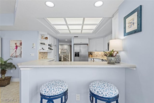 kitchen featuring backsplash, a peninsula, white cabinets, and stainless steel fridge with ice dispenser