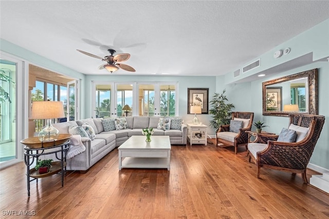 living room with french doors, a textured ceiling, visible vents, and hardwood / wood-style floors