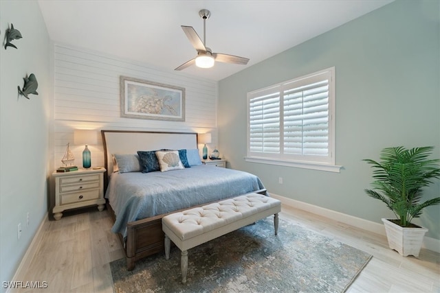 bedroom with ceiling fan, an accent wall, baseboards, and wood finished floors