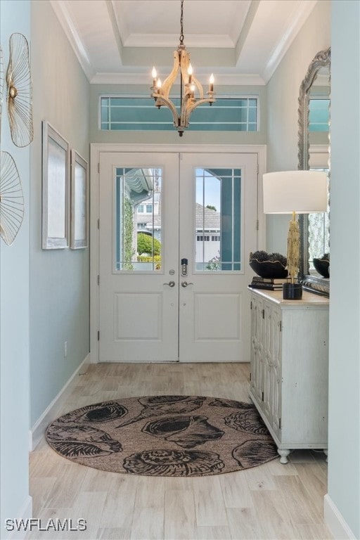 foyer with light wood finished floors, ornamental molding, a raised ceiling, and a notable chandelier