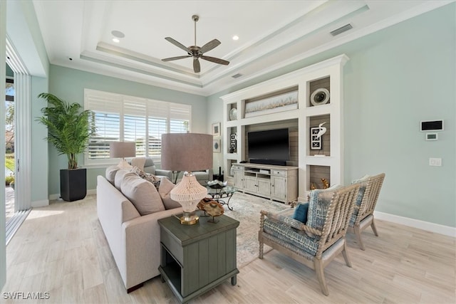 living area with a tray ceiling, light wood finished floors, visible vents, ornamental molding, and baseboards