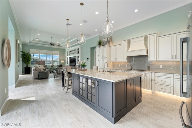 kitchen featuring black electric stovetop, open floor plan, tasteful backsplash, a raised ceiling, and custom range hood