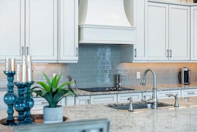 kitchen featuring premium range hood, white cabinetry, backsplash, and a sink