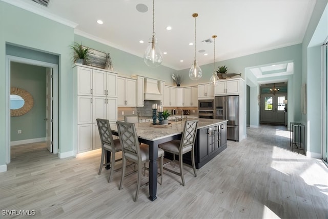 kitchen with light wood finished floors, custom range hood, appliances with stainless steel finishes, ornamental molding, and backsplash