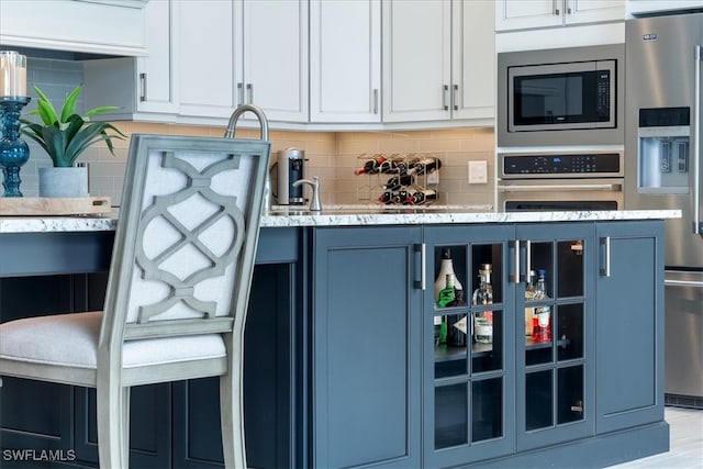 kitchen with appliances with stainless steel finishes, blue cabinets, glass insert cabinets, and decorative backsplash