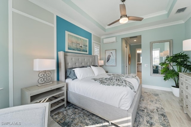 bedroom with a wall unit AC, light wood-style flooring, baseboards, a raised ceiling, and crown molding