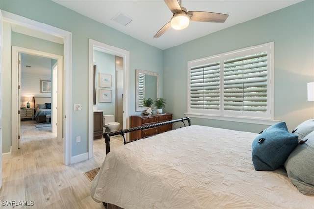 bedroom featuring light wood finished floors, visible vents, baseboards, ensuite bath, and ceiling fan