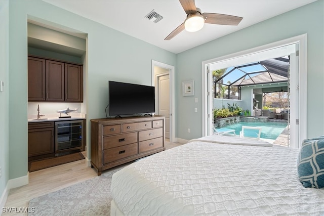 bedroom featuring wine cooler, a sunroom, baseboards, access to outside, and light wood-type flooring