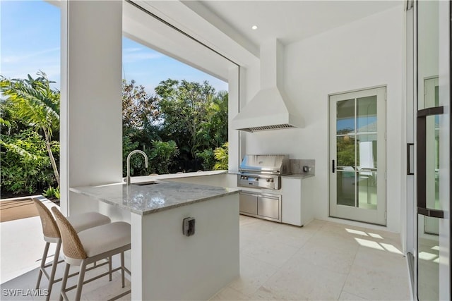 kitchen with light stone counters, a breakfast bar area, a sink, white cabinetry, and custom exhaust hood