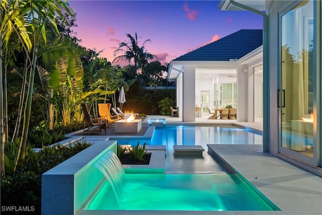 pool at dusk with a patio area, an outdoor pool, and a fire pit