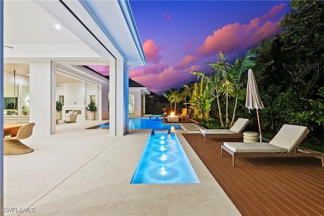 pool at dusk with an outdoor pool and a wooden deck