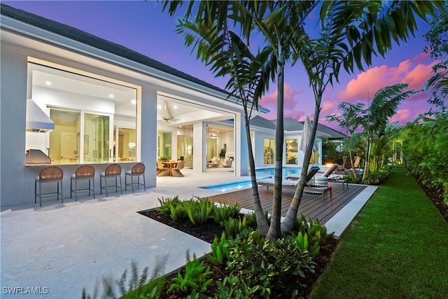 pool at dusk featuring an outdoor pool, a patio, ceiling fan, outdoor dry bar, and a yard