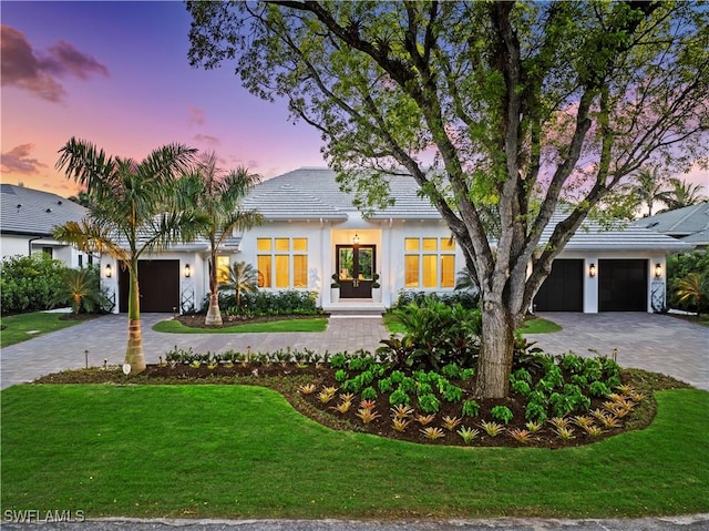 modern inspired farmhouse with decorative driveway, an attached garage, a front lawn, and stucco siding