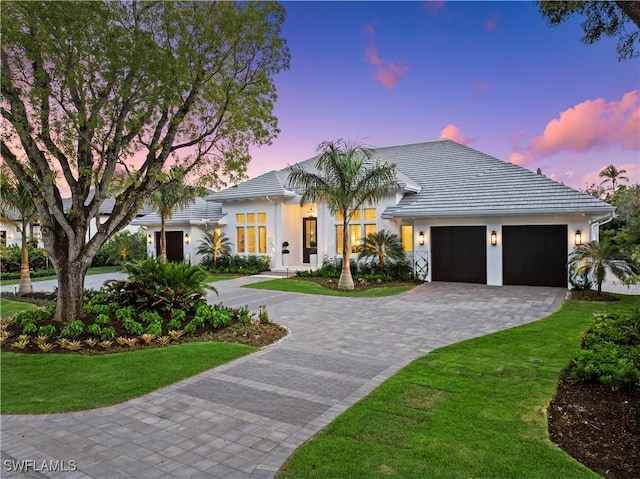 modern farmhouse style home with a garage, decorative driveway, a yard, and stucco siding