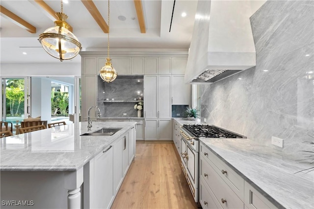 kitchen featuring stainless steel stove, decorative backsplash, light wood-style floors, a sink, and wall chimney range hood