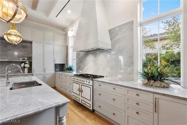 kitchen featuring light wood-style flooring, a sink, decorative backsplash, light stone countertops, and custom range hood