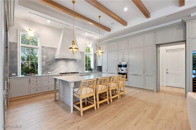 kitchen with tasteful backsplash, custom range hood, gray cabinetry, light wood-style floors, and appliances with stainless steel finishes