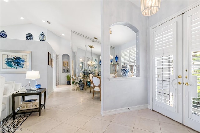 entrance foyer featuring arched walkways, light tile patterned floors, baseboards, a chandelier, and vaulted ceiling