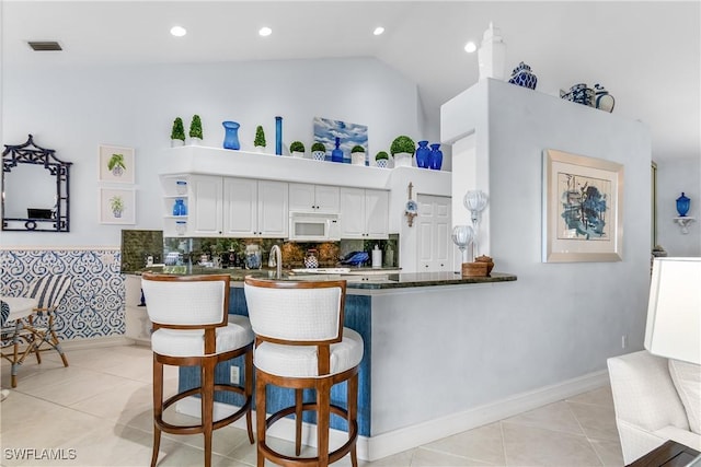 kitchen featuring light tile patterned floors, visible vents, white microwave, and dark countertops