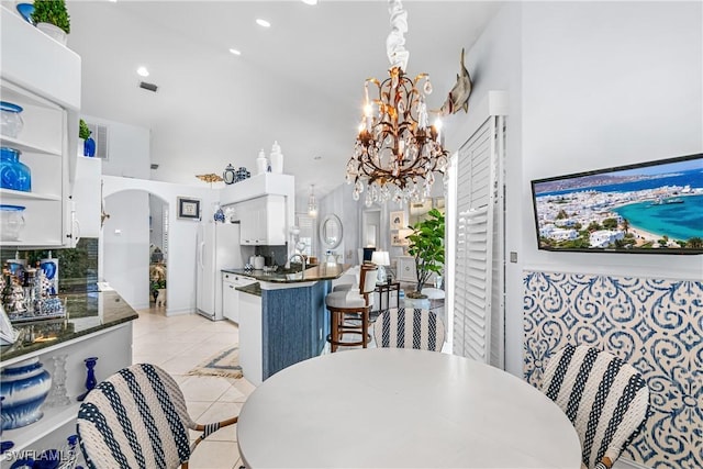 dining space featuring arched walkways, a notable chandelier, a high ceiling, and light tile patterned floors