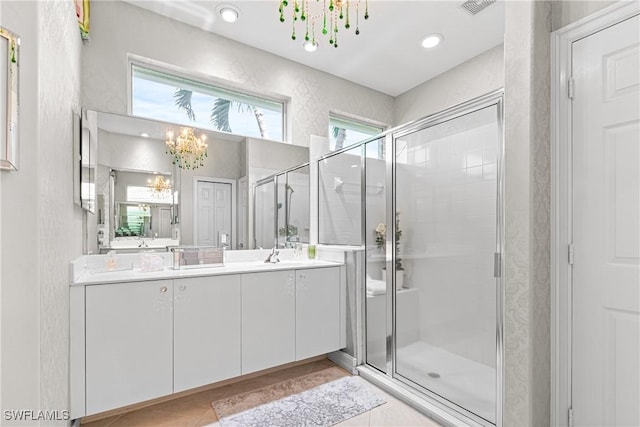 bathroom featuring a shower stall, a notable chandelier, double vanity, and a sink