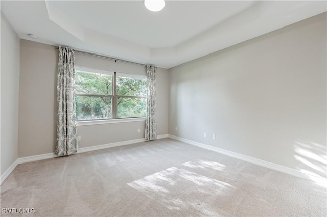 carpeted empty room featuring a tray ceiling and baseboards