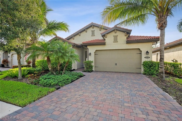 mediterranean / spanish-style home with a garage, a tiled roof, decorative driveway, and stucco siding