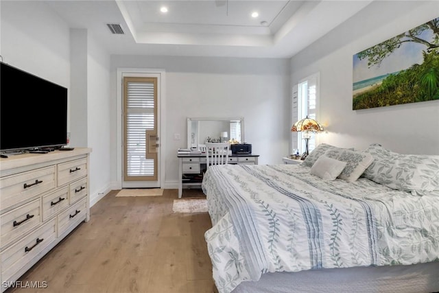 bedroom featuring light wood finished floors, a raised ceiling, visible vents, and baseboards