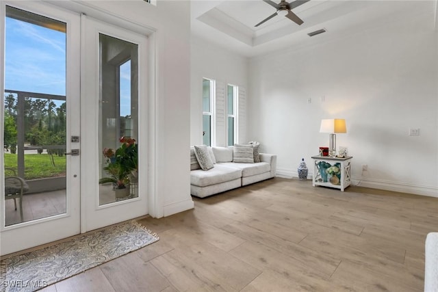 interior space featuring ceiling fan, light wood-style flooring, visible vents, baseboards, and a tray ceiling