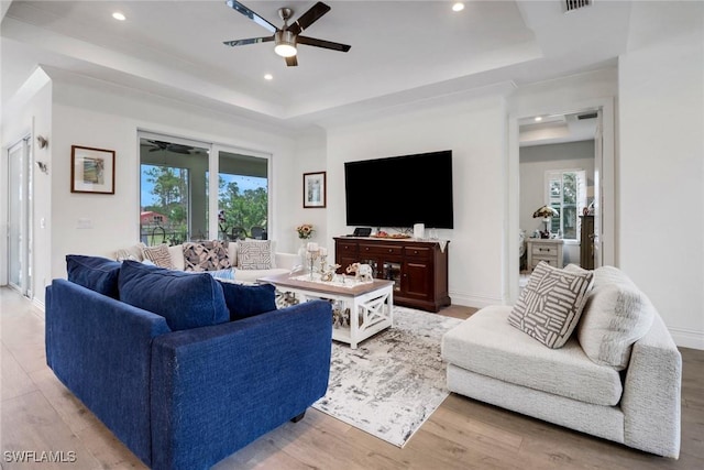 living room featuring ceiling fan, a tray ceiling, and a wealth of natural light