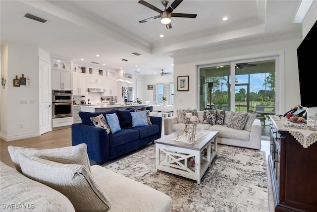 living area featuring light wood-style floors, visible vents, a tray ceiling, and recessed lighting